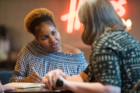 Image of a black lady sat talking to another lady who has her back to us