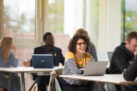 Image of a white lady smiling up from her computer with other people sat nearby