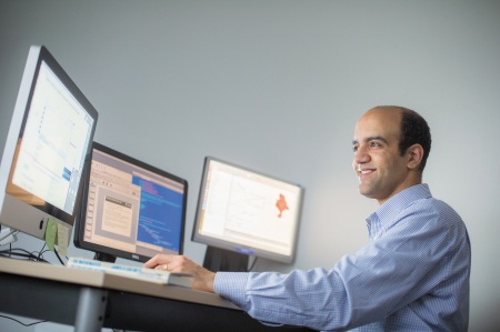 A man smiling and looking at one of three monitors